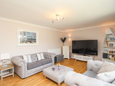 A living room with two grey sofas a large flat screen TV a white side table and wooden bookshelf at The White House in Weymouth
