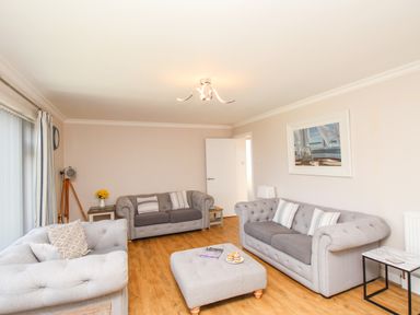 A living room with three grey sofas a central ottoman a side table with flowers and a painting on the wall at The White House in Weymouth