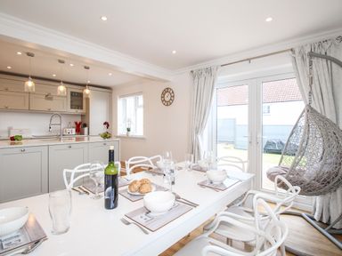 A dining area with a set table and kitchen in the background at The White House in Weymouth