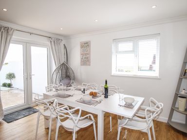 A dining room with a white table set with bowls glasses and cutlery white chairs a hanging chair near glass doors and a window at The White House in Weymouth