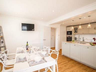 A kitchen with a dining table set with bowls and glasses next to an island counter with a sink at The White House in Weymouth