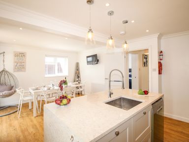A kitchen island with a sink and hanging lights overlooking a dining table with chairs and a hanging chair in a white room at The White House in Weymouth
