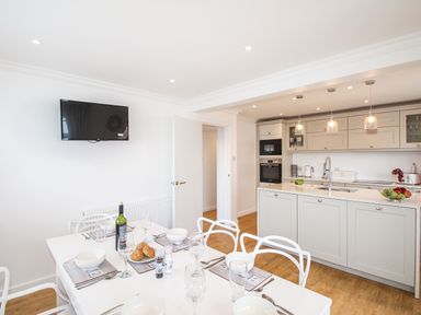 A kitchen and dining area with white cabinets and table set with bowls and glasses at The White House in Weymouth