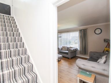 A striped carpeted staircase next to a living room with grey sofas and a clock on the wall at The White House in Weymouth