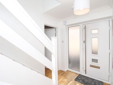 An entryway with a white front door a glass side panel a gray doormat wooden flooring and white stairs at The White House in Weymouth