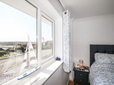 A bedroom with a bed a nightstand a decorative sailboat on the windowsill and a window with curtains at The White House in Weymouth