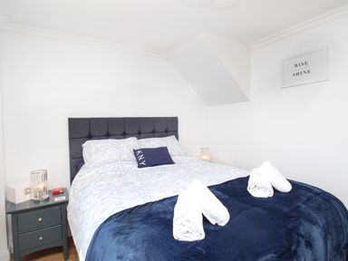 A bedroom with a double bed with a dark headboard and white and blue bedding with rolled towels on the bed at The White House in Weymouth