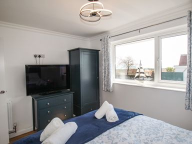 A bedroom with a bed, chest of drawers, wardrobe, television, and a window with curtains at The White House in Weymouth