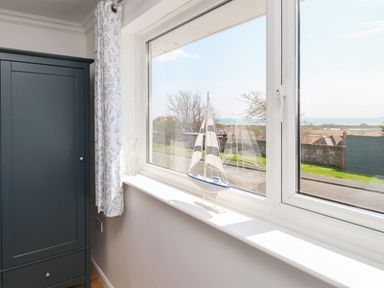 A window with a model sailboat on the sill next to a dark wardrobe and floral curtains at The White House in Weymouth