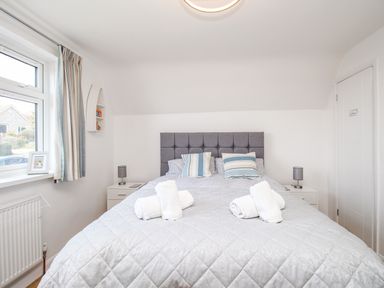 A bedroom with a bed with grey quilt and striped pillows two rolled towels on the bed bedside tables with lamps and a window with curtains at The White House in Weymouth