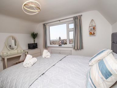 A bedroom with a bed with striped pillows a dresser with a mirror a small television and a window with curtains at The White House in Weymouth