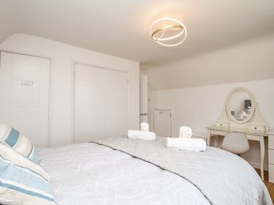 A bedroom with a bed, rolled towels, a dressing table with an oval mirror, and white doors at The White House in Weymouth