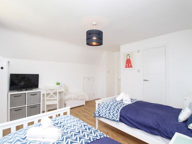 A bedroom with two single beds blue bedding a TV on a dresser a white desk and chair and wooden floor at The White House in Weymouth