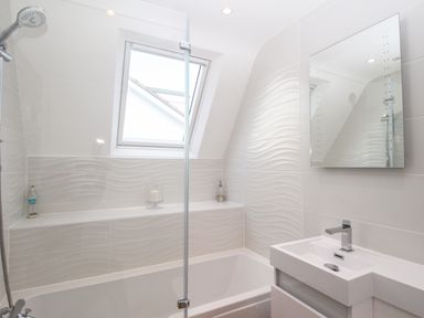 A bathroom with a bathtub a showerhead a sink with a faucet a mirror and a window at The White House in Weymouth