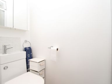A bathroom with a toilet a small sink a towel ring with a blue towel a white tissue holder and a wicker storage unit at The White House in Weymouth