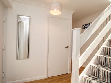 A hallway with a white door a wall mirror and carpeted stairs with a striped pattern at The White House in Weymouth