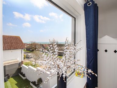A window with a vase of white flowers on the sill and a view of rooftops and the sea at The White House in Weymouth