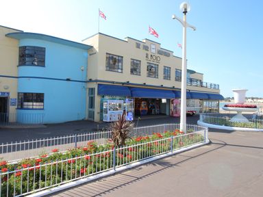 A building with a blue and cream facade with signs for al molo italian fine dining and the pier bandstand with flower beds and a lamppost outside at The White House in Weymouth