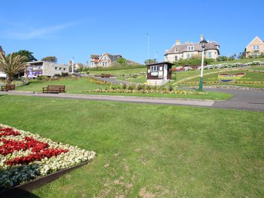 A garden with flower beds benches a small building and houses in the background at The White House in Weymouth