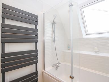 A bathroom with a bathtub shower combination towel radiator and a window at The White House in Weymouth