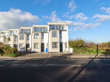 A row of three story modern white houses with balconies and a road in front at Chy Fistral in Newquay