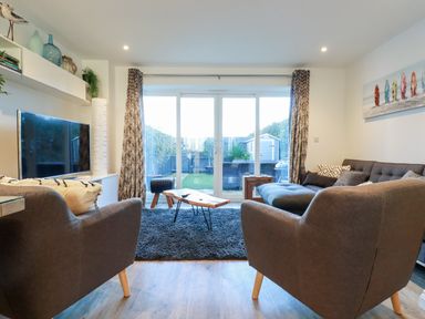 A living room with two armchairs a sofa a coffee table and a television with sliding glass doors leading to a garden at Chy Fistral in Newquay