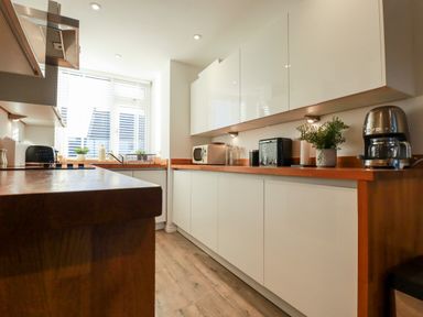 A kitchen with white cabinets wooden countertops appliances and a window with blinds at Chy Fistral in Newquay