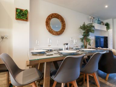 A dining area with a glass top table set for six with plates and wine glasses at Chy Fistral in Newquay