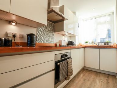A kitchen with white cabinets wooden countertops kettle toaster and oven with window blinds at Chy Fistral in Newquay