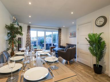 A dining table set with plates and glasses next to a living area with a gray couch and plants at Chy Fistral in Newquay
