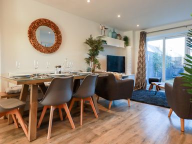 A dining area with a table set for four and a living room with armchairs and a television at Chy Fistral in Newquay