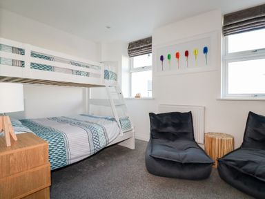 A bedroom with a bunk bed two black bean bag chairs a wooden bedside table and colorful artwork on the wall at Chy Fistral in Newquay