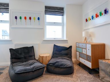 A room with two black bean bag chairs a wooden side table a wooden cabinet with patterned drawers and colorful wall art at Chy Fistral in Newquay