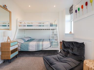 A bedroom with a bunk bed two drawers a lamp a chair and a window at Chy Fistral in Newquay
