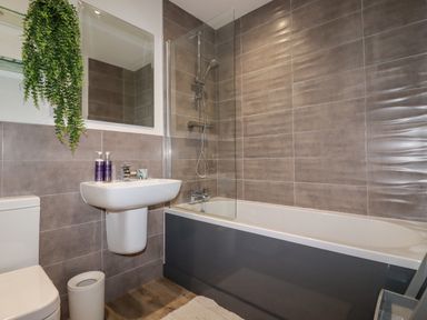 A bathroom with a bathtub shower combo a sink a toilet and a hanging plant at Chy Fistral in Newquay