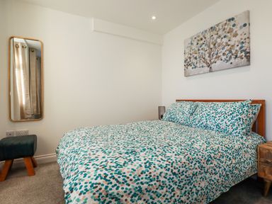 A bedroom with a bed with patterned bedding a wall mirror a small bench and a painting above the bed at Chy Fistral in Newquay