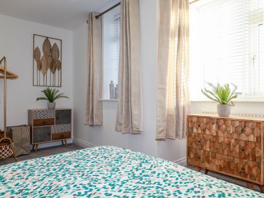 A bedroom with patterned bedspread two dressers plants on top and beige curtains at Chy Fistral in Newquay