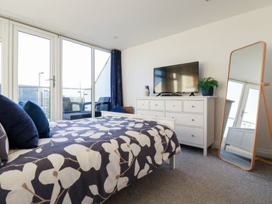 A bedroom with a bed a dresser a mirror and glass doors leading to a balcony at Chy Fistral in Newquay