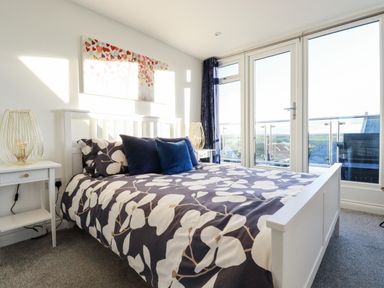 A bedroom with a white bed and floral bedding next to glass doors leading to a balcony at Chy Fistral in Newquay