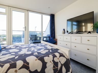 A bedroom with a bed in front of large glass doors and a white dresser with a television on top at Chy Fistral in Newquay