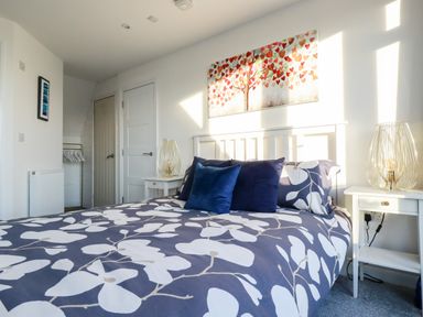 A bedroom with a bed with floral bedding and two bedside tables with lamps at Chy Fistral in Newquay