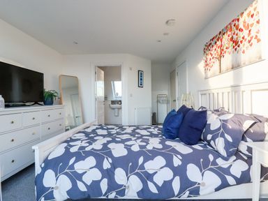 A bedroom with a white bed floral bedding blue pillows and a dresser with a television and a mirror at Chy Fistral in Newquay