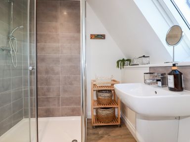 A bathroom with a shower, sink, storage shelves with baskets, and a small mirror at Chy Fistral in Newquay