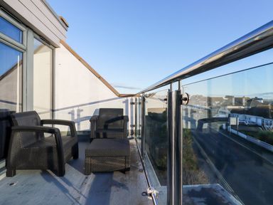 A balcony with two black chairs and a black table with glass railing overlooking a street at Chy Fistral in Newquay