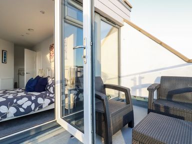 A bedroom with a bed and pillows visible through an open door to a balcony with outdoor chairs at Chy Fistral in Newquay