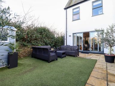 An outdoor patio with plastic furniture on artificial grass next to a white house with sliding glass doors at Chy Fistral in Newquay