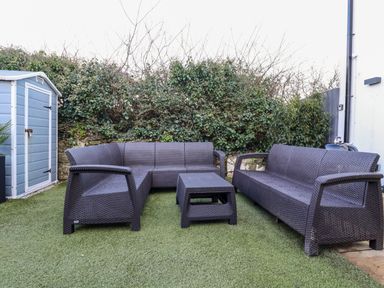 An outdoor seating area with rattan style furniture and a small storage shed at Chy Fistral in Newquay