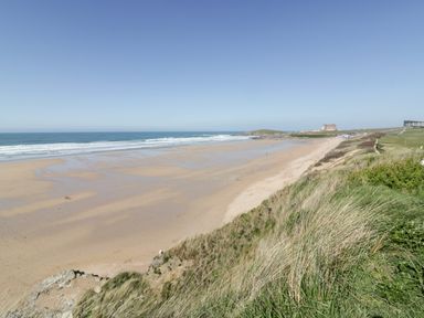 A sandy beach with ocean waves and grassy cliffs in the foreground at Chy Fistral in Newquay