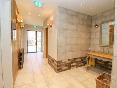 A hallway with tiled floor and walls with a wooden table and mirror in a corner at The Piggery in Ledbury near Welland