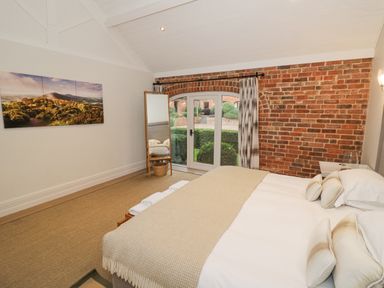 A bedroom with a bed near glass doors and brick wall with a standing mirror at The Piggery in Ledbury near Welland